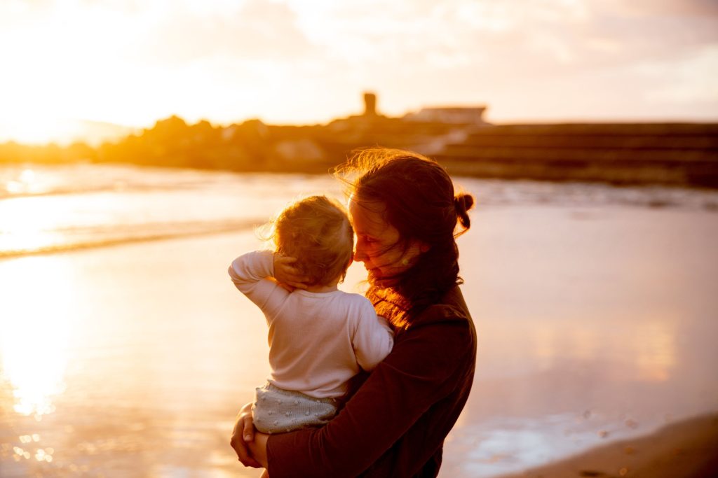Mãe segurando o filho na praia ao pôr do sol